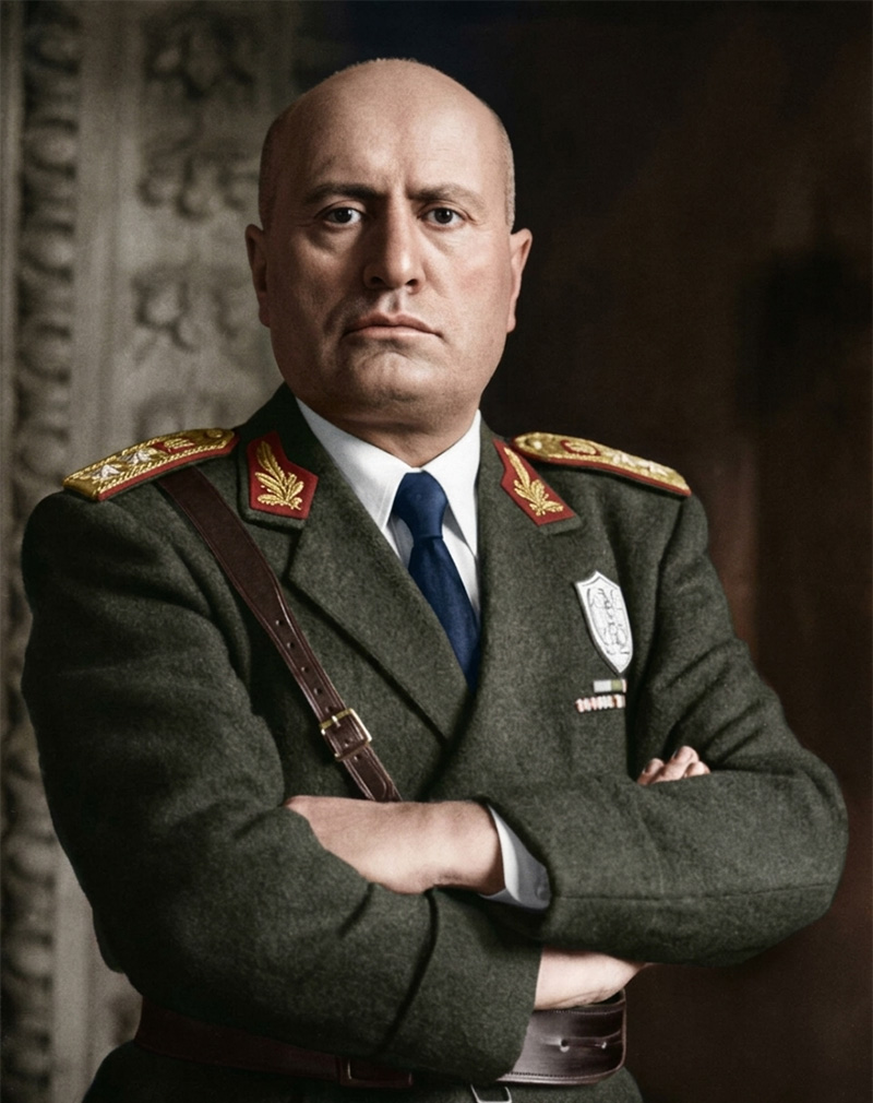 腕を組み威圧的な表情でこちらを睨む、イタリアの独裁者ムッソリーニのカラー写真。ファシズムの台頭を象徴する一枚。