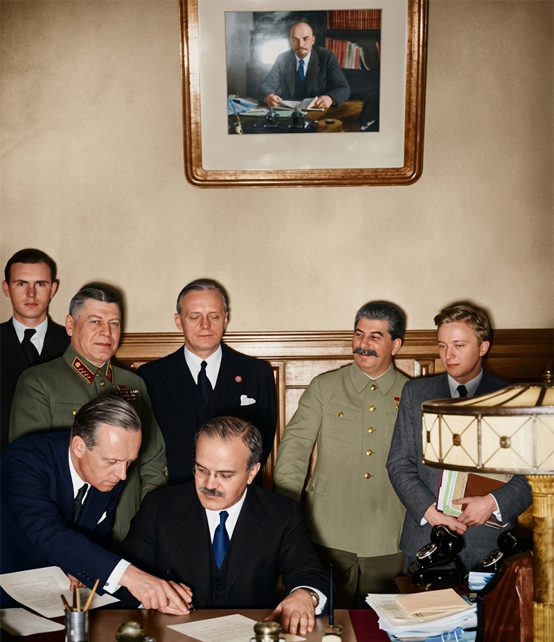 1939年、モスクワで独ソ不可侵条約に署名するソ連のモロトフ外相と、その後ろで見守るドイツのリッベントロップ外相、ソ連のスターリン最高指導者らのカラー復元写真。壁にはレーニンの肖像画が掛かっている。