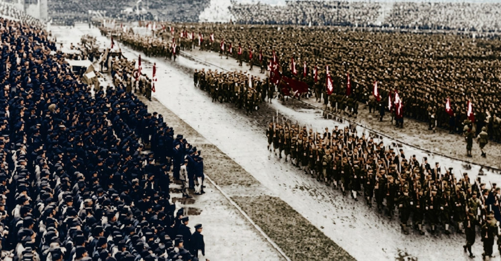 1943年、雨の明治神宮外苑競技場で行われた学徒出陣壮行会で、銃を肩に行進する学生兵たちの列と、それを見守る超満員の観衆。
