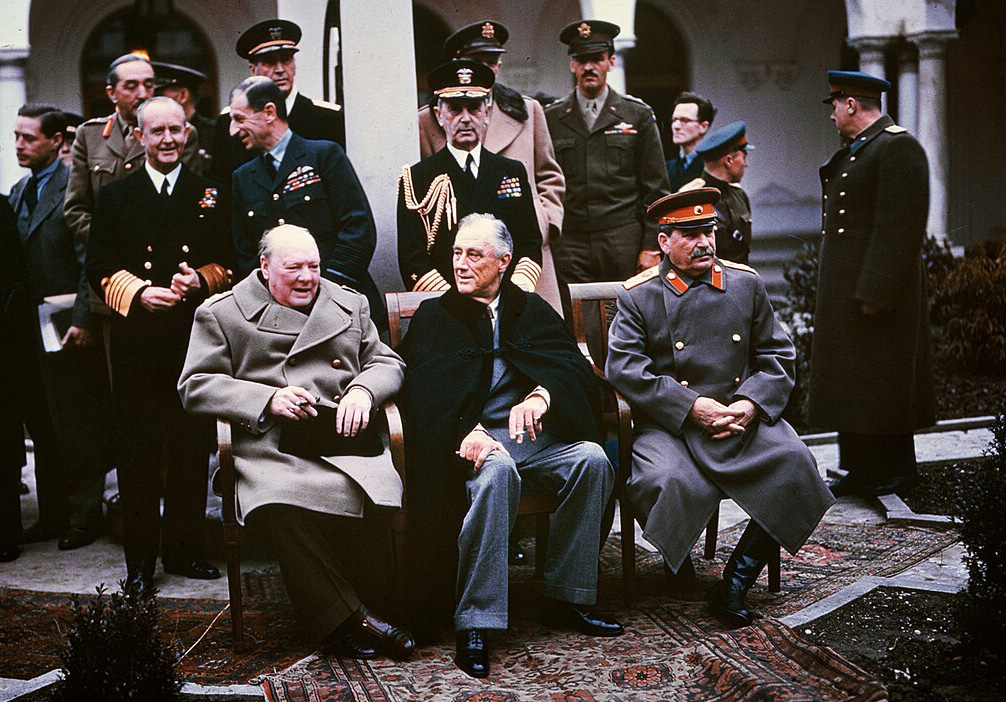 1945年のヤルタ会談にて、リヴァディア宮殿の中庭で椅子に座るイギリス首相チャーチル、アメリカ大統領ルーズベルト、ソ連書記長スターリン。背後には軍関係者や政府高官たちが立っている。