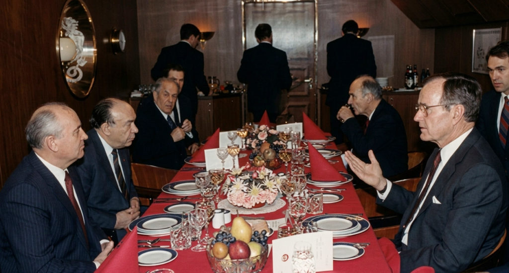 1989年のマルタ会談中、ソ連のゴルバチョフ書記長とアメリカのブッシュ大統領が豪華な夕食会のテーブルを挟んで対話している様子。