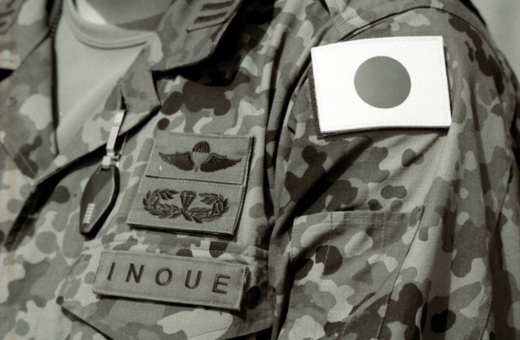 日本の陸上自衛隊員の迷彩制服の左胸。日本国旗パッチ、空挺バッジ、特殊部隊バッジ、そして『INOUE』という名札が見える。